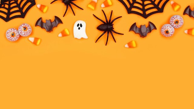 Halloween top border of scattered candy and decor. Above view stop motion video over an orange background with copy space.