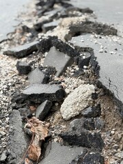 Cracked asphalt road with fallen leaves and pebbles, depicting urban decay and infrastructure issues