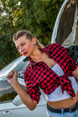 Beautiful girl in a checkered shirt with a wrench in her hands stands against the background of an...