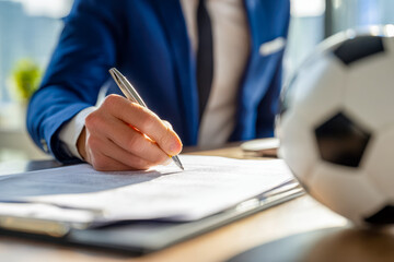 Person in formal attire signing documents with a soccer ball nearby