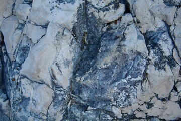 Close-up of a rock surface with cracks and textured patterns. Gray and white shades of the stone highlight the natural texture and details of the mountain rock.