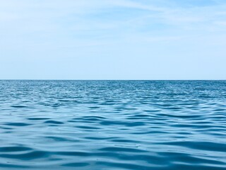 The serene blue sea stretches to the horizon under a clear sky. Gentle waves reflect the light, creating a peaceful and calming atmosphere.