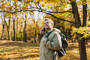 Happy 30s man talking on smartphone. Technology mobile cellphone. Young caucasian male smiling happy talking on the smartphone at the park. Autumn season. High quality photo