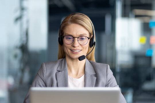 Smiling businesswoman with headset working on laptop in modern office