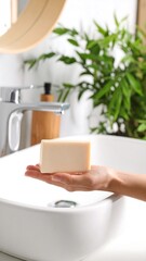 Hand holding bar of soap in bathroom sink