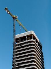 Building cranes dominate construction site. Tall concrete skyscraper rises in urban development,