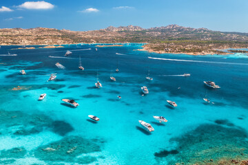 Obraz premium Aerial view of luxury yachts and boats on blue sea, beautiful island, mountain on summer sunny day. Sandy beach, rocky sea coast, azure transparent water in Sardinia, Italy. Top drone view. Seascape