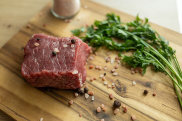 close up of a piece of fresh beef on a wooden cutting board. farm fresh meat with coarse salt and...
