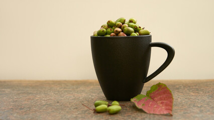 A black cup filled with actinidia kolomikta berries on a table. Nearby is a red leaf of the plant and several scattered berries. Copy space.