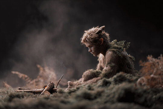 A solitary, horned faun sits pensively by a small fire in a dark forest, symbolizing isolation, mythology, or fantasy. Evokes a sense of mystery, longing, and the wild.