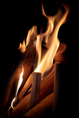 A fire of neat, cleaned wood flares up in the darkness. The flames spread to new logs