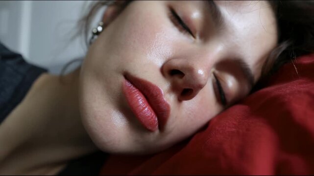 Young woman lying sideways on a red pillow with half-open eyes, giving the impression of tiredness or drowsiness