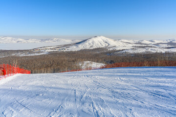 Steep ski slope with red restrictive net against the backdrop of picturesque Ural Mountains...