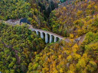 Žampach Railway Viaduct in Jílové u Prahy, Czech Republic. Aerial view of the historic stone bridge surrounded by forest in vibrant autumn colors.