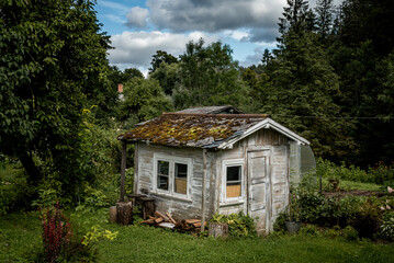 Old small rustic house surrounded by trees. The weathered wooden building with a worn appearance...