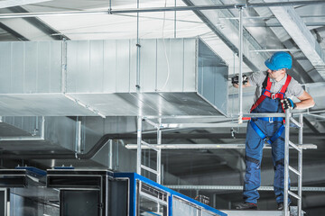 Construction HVAC Worker Installing Air Duct in Warehouse During Daylight Hours
