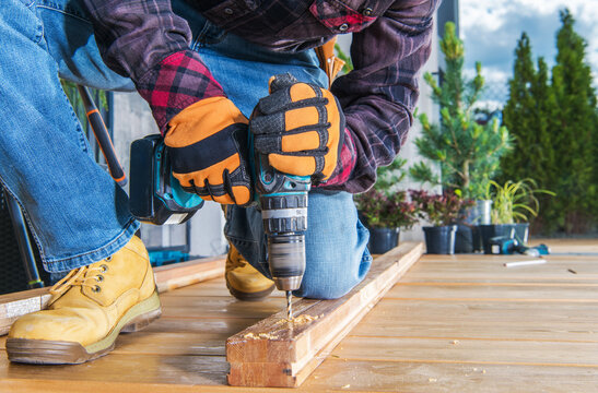 Man Using Electric Drill on Wooden Plank While Working Outdoors