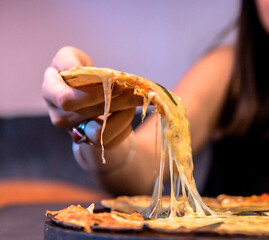 A woman's hand pulling a piece of thin crust cheesy, delicious Margherita Pizza to eat. Lots of...