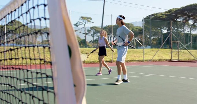 Jogging Diverse tennis players approaching net on hard court, exchanging rackets and shaking hands