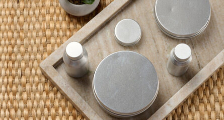 Skin care items silver metal bottles and jars on a marble tray.