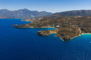 Obraz premium Aerial view of Voulisma Beach in Crete, Greece, featuring turquoise waters, golden sand, rugged coastline, arid hills, and distant mountains.