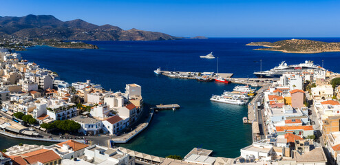Aerial view of Agios Nikolaos, Crete, showing a vibrant harbor with yachts, whitewashed buildings,...