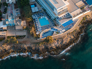 Aerial view of a modern resort in Stalida, Crete, with a large pool, sun loungers, and umbrellas by...