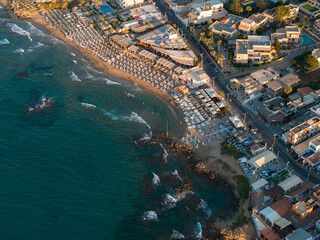 Aerial view of Stalida, Crete, showing a vibrant beachfront with sun loungers, turquoise...