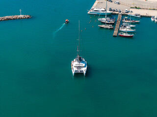 Aerial view of a marina in Rethymno, Crete, featuring a catamaran in turquoise waters, moored...