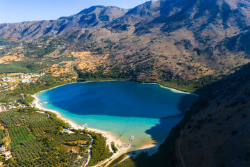 Aerial view of Lake Kournas in Crete, Greece, showing turquoise waters, small boats, rugged...
