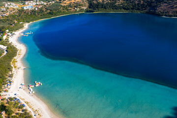 Aerial view of Lake Kournas in Crete, Greece, featuring deep blue and turquoise waters, a sandy...