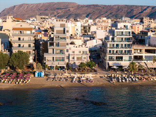 Coastal area in Chania, Crete, with buildings facing a sandy beach lined with loungers and...