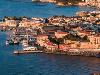 Aerial view of Chania town, Crete, Greece, featuring the Venetian Harbor, colorful waterfront buildings, docked boats, and a golden sunset glow.