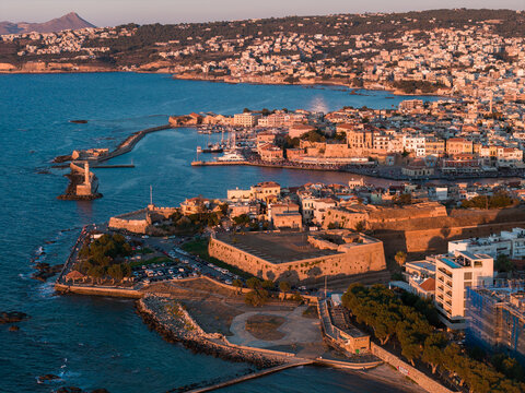 Aerial view of Chania, Crete, Greece, featuring the Venetian Harbor, iconic lighthouse, historic architecture, and golden sunset over the sea. - Powered by Adobe