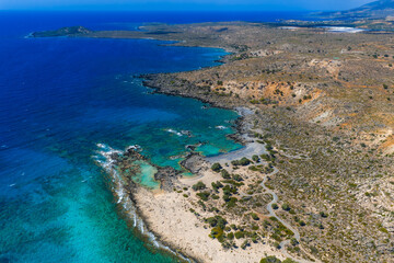 Fototapeta premium Aerial view of Elafonisi Beach in Crete, Greece, showing turquoise waters, sandy beaches, rugged terrain, and distant islands along the coastline.