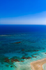 Aerial view of Elafonisi Beach in Crete, Greece, showing turquoise waters, coral reefs, sandbars, and a sandy shoreline in the lower right corner.