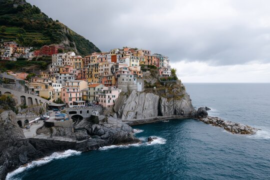 Picturesque village perched on rugged cliffside overlooking the sea on a cloudy day. Coastal town architecture for travel and real estate.