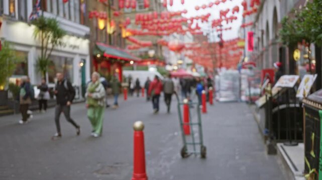 People walking in defocused london chinatown street during autumn with blurred background and red lanterns overhead creating a vibrant outdoor scene