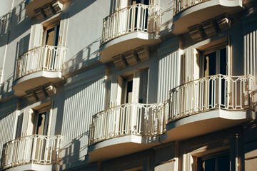 A building with elegant balconies and architectural details in a light. Facade with balconies, ornate railings, and open shutters on the windows. Classic European (Spanish) architecture.