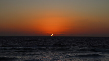Pôr do sol sobre o mar, com o horizonte iluminado em tons alaranjados refletindo nas águas, criando cenário romântico e natural inesquecível