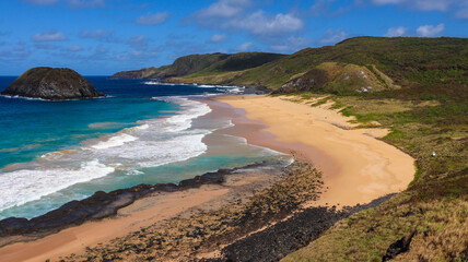 Visão aérea da Praia do Leão, Noronha, com águas turquesa, areia dourada, ondas suaves e...