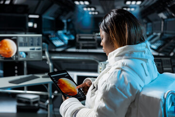 Astronaut prepares for space travel operations, reading Mars expedition status on device. Spaceman wearing spacesuit inside futuristic spacecraft monitoring red planet surface scan data on tablet