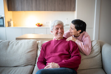 Old married man and woman laughing talking on couch at home, engaging in cheerful conversation....