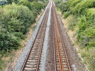 Parallel railway tracks extending into the distance surrounded by greenery and bushes. Concept of travel, transportation, journey, direction, and connection. Captured from above, showing perspective