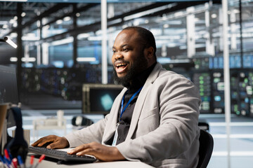 Cheerful software developer in data center checking infrastructure health report showing stable...