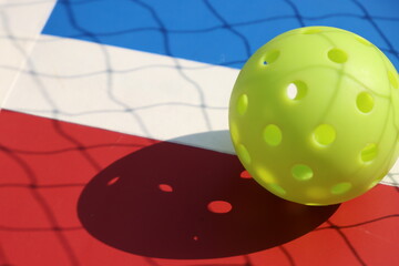 Pickleball ball in the court floor with red and blue colors with a net shadow
