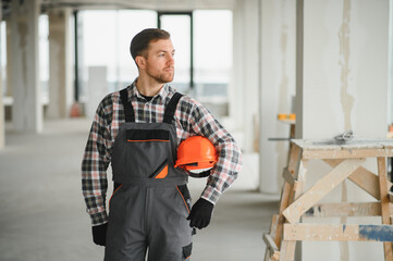 Construction worker holding helmet and inspecting building site