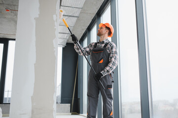 Construction worker painting walls with roller in building renovation project