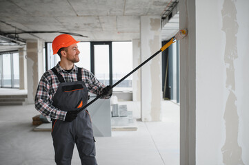 Construction worker painting walls with roller in building renovation