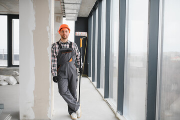 Construction worker holding paint roller near window in building under construction